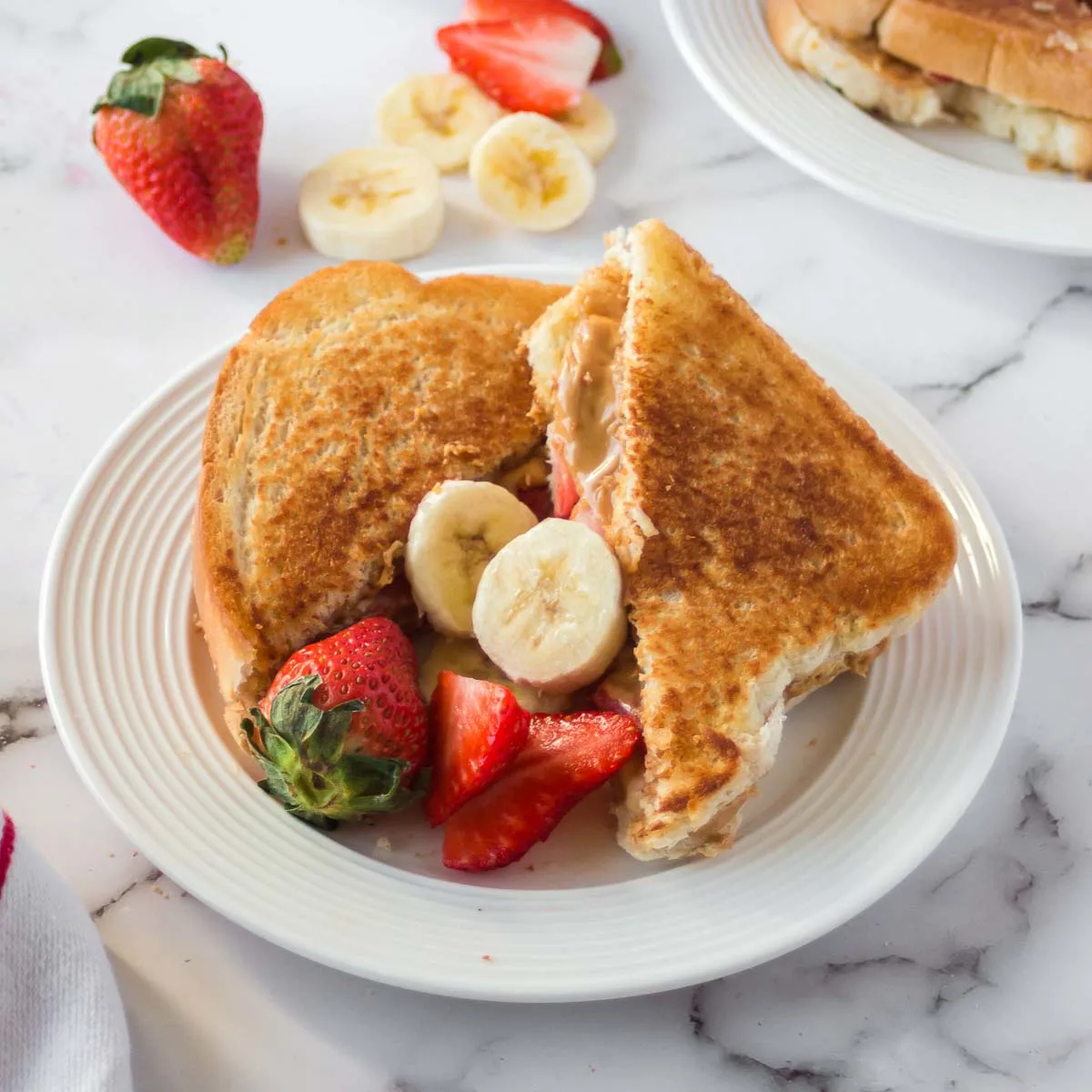 Grilled peanut butter sandwich sliced on a plate with fresh strawberries and banana.