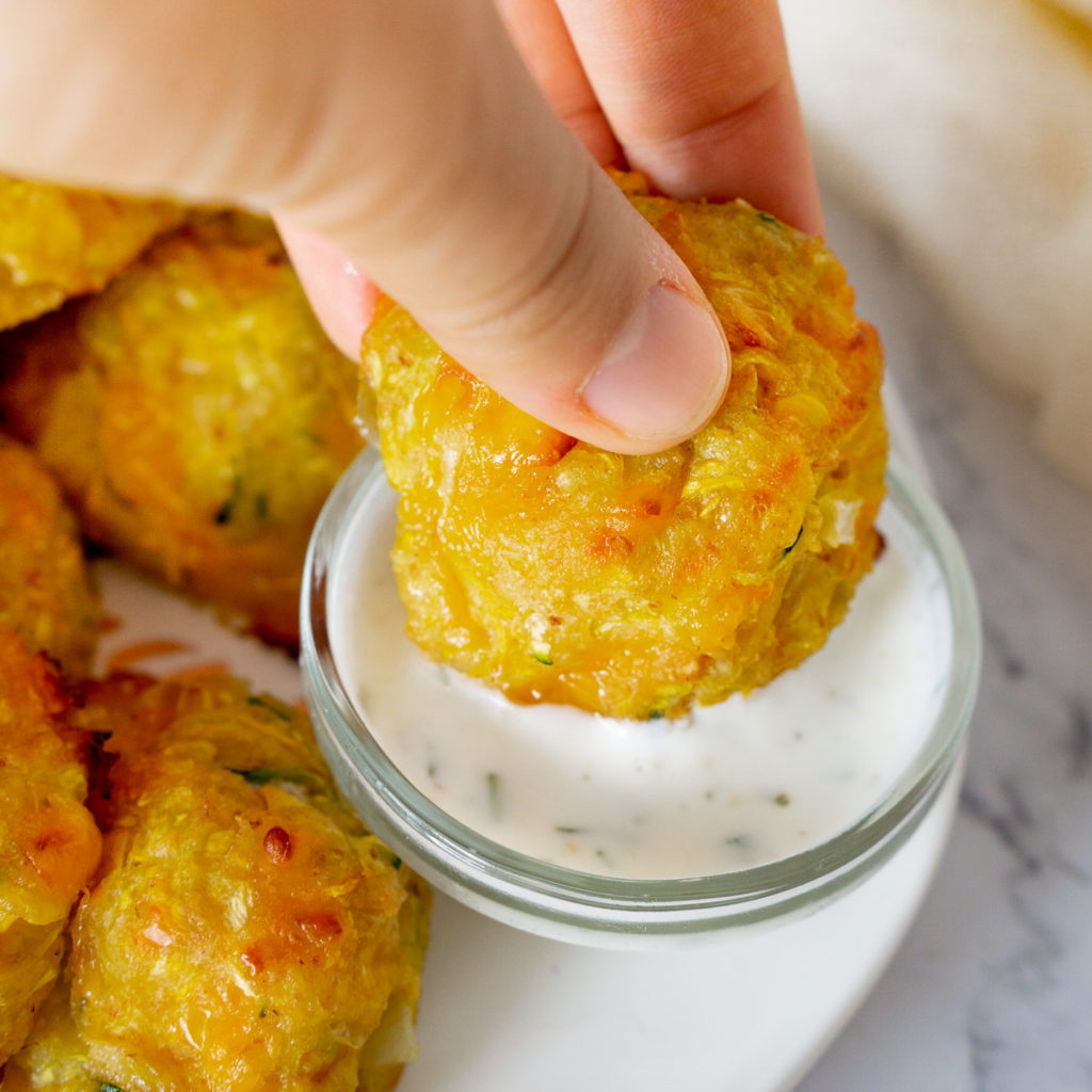 dipping yellow squash tots into a dip