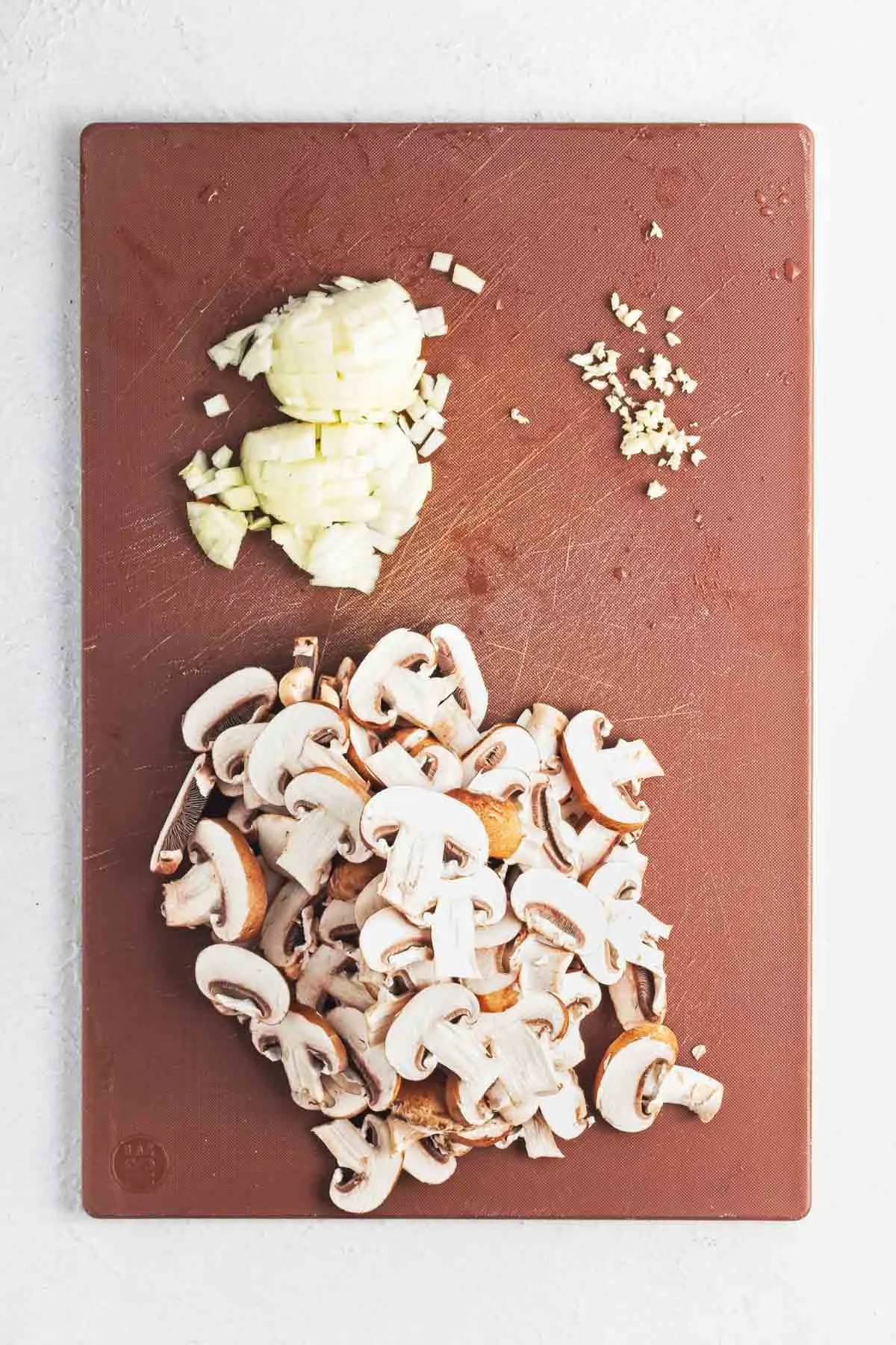 Sliced mushrooms, diced onion, and minced garlic on a cutting board