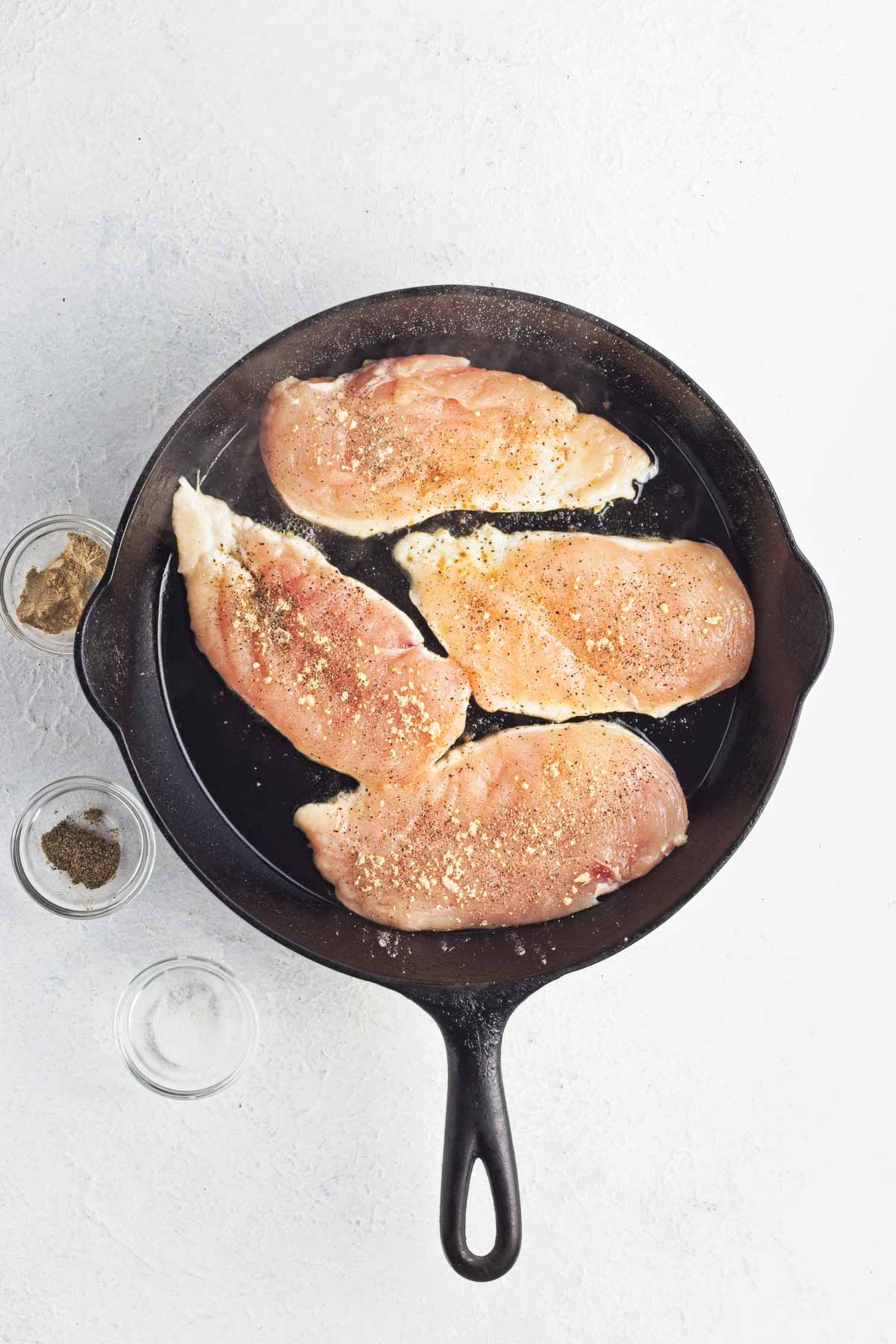 Thin-sliced chicken breasts cooking in a skillet, seasoned on top