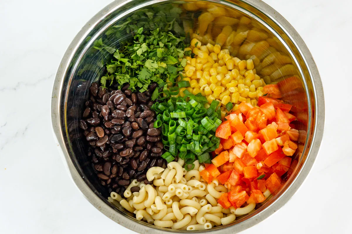 ingredients for mexican macaroni salad in a bowl: corn, black beans, tomato, cilantro, macaroni