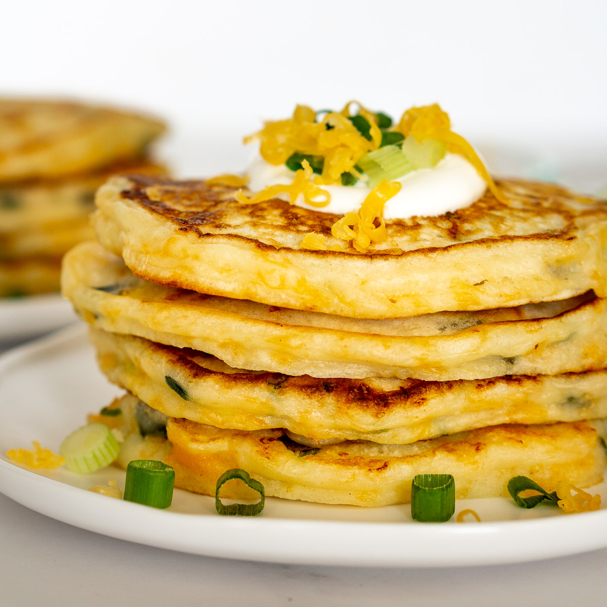 stack of savory cheesy pancakes topped with sour cream