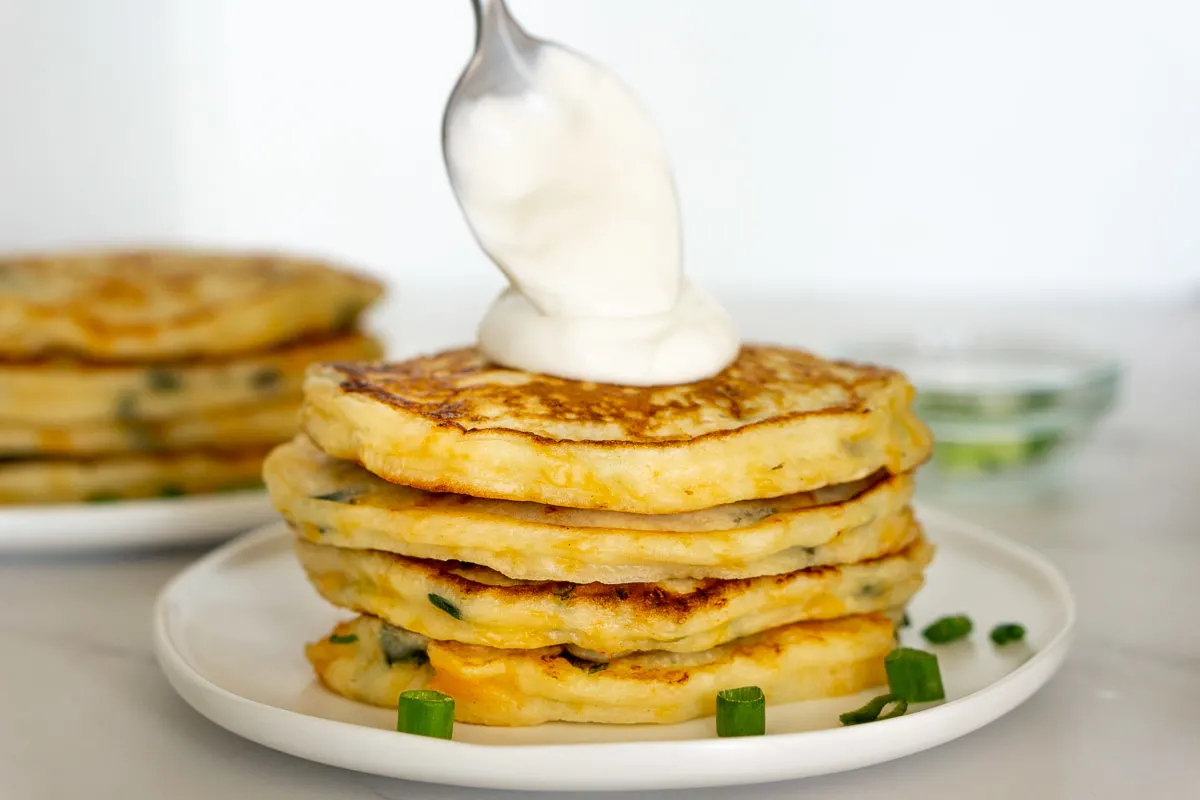 spooning lime crema onto a stack of savoury pancakes