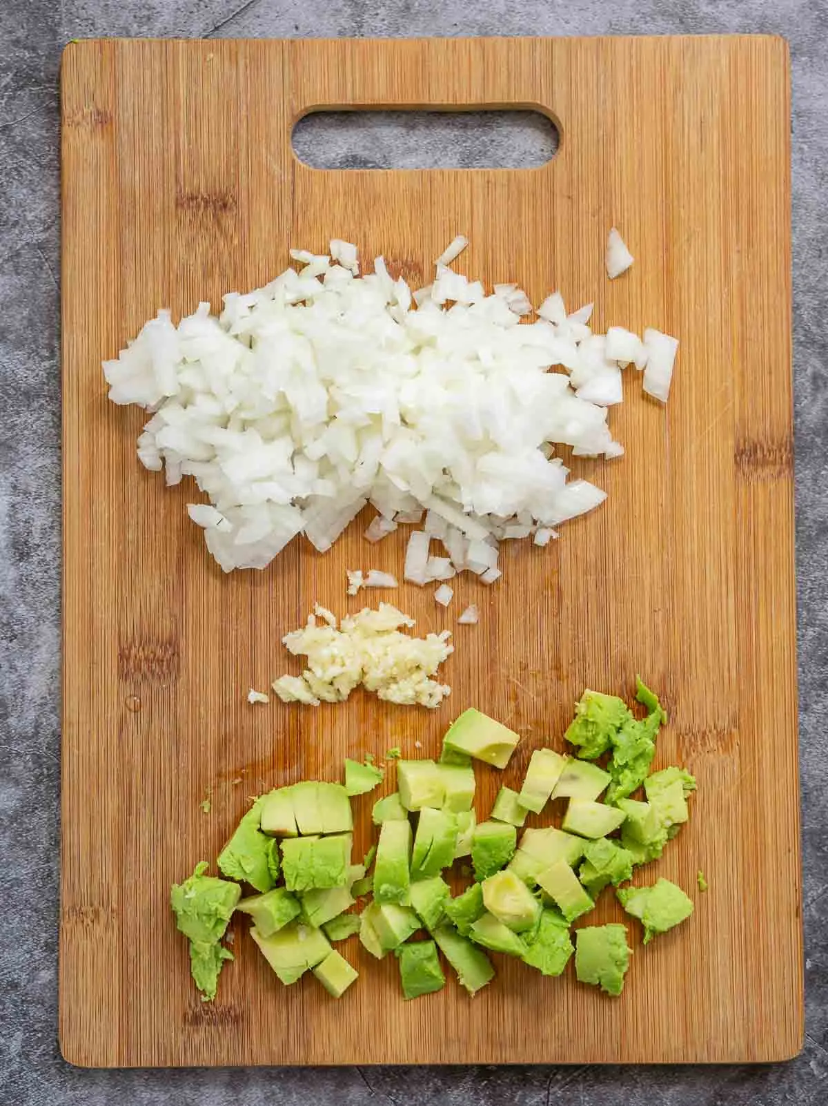 Dice onion, pressed garlic, and diced avocado on a cutting board.