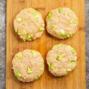 Uncooked chicken burger patties with pieces of avocado.