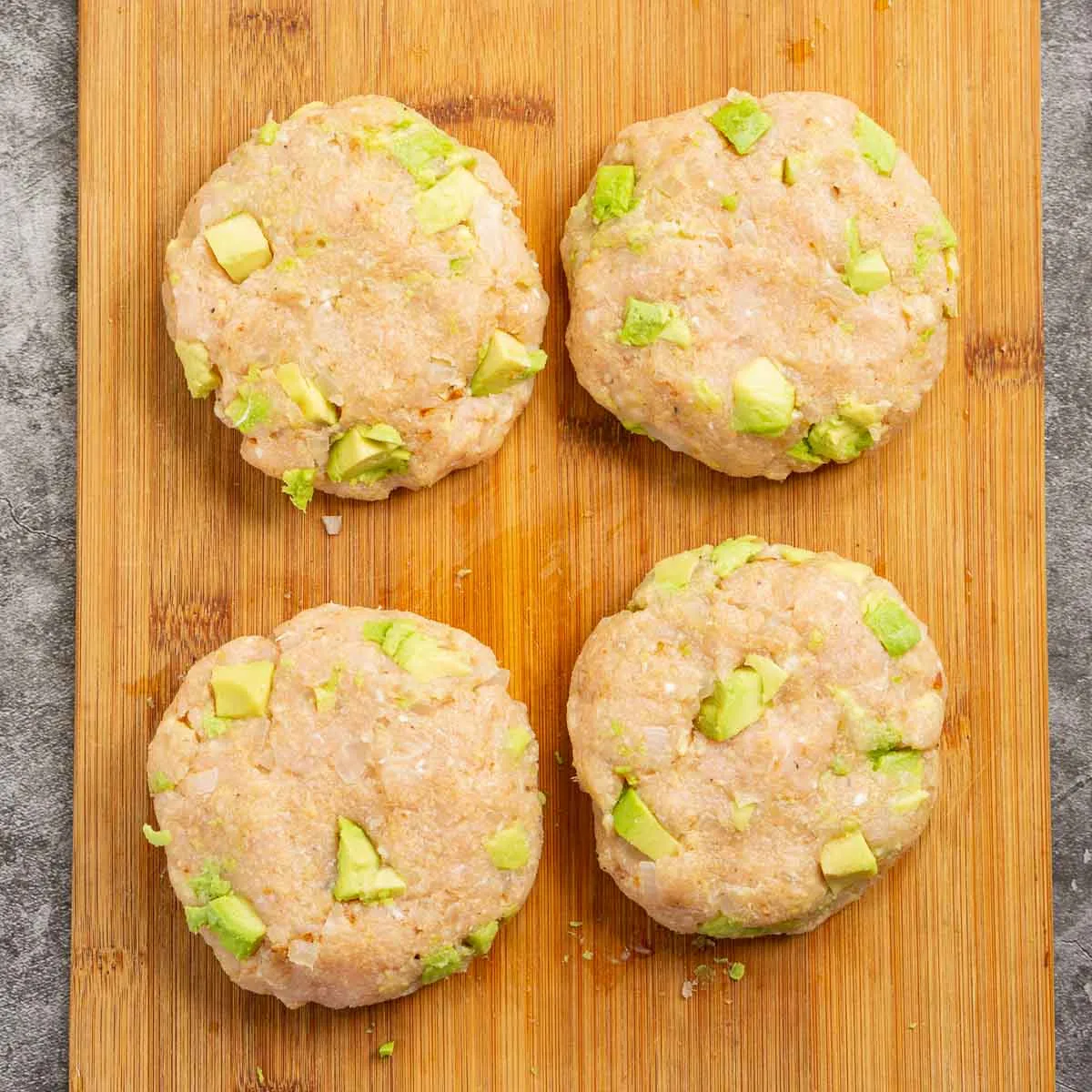 Uncooked chicken burger patties with pieces of avocado.