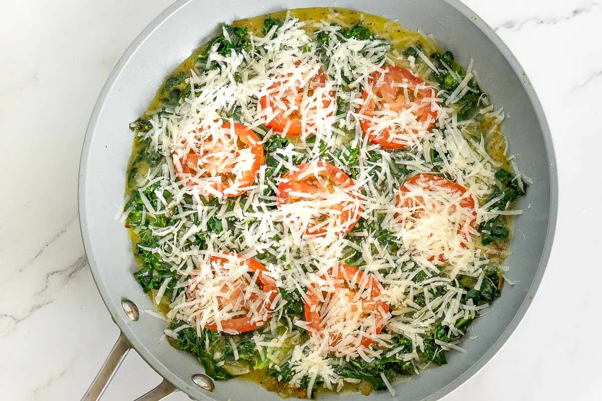Kale, tomato, egg, and parmesan cheese in a pan.