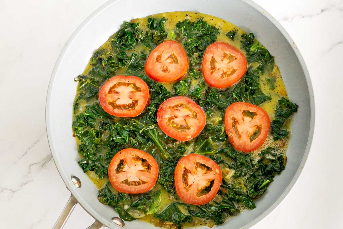 Sliced tomatoes on top of sauteed kale in a pan.