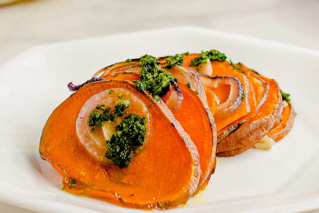 Close up of a serving of sweet potato tian on a plate topped with parsley sauce.