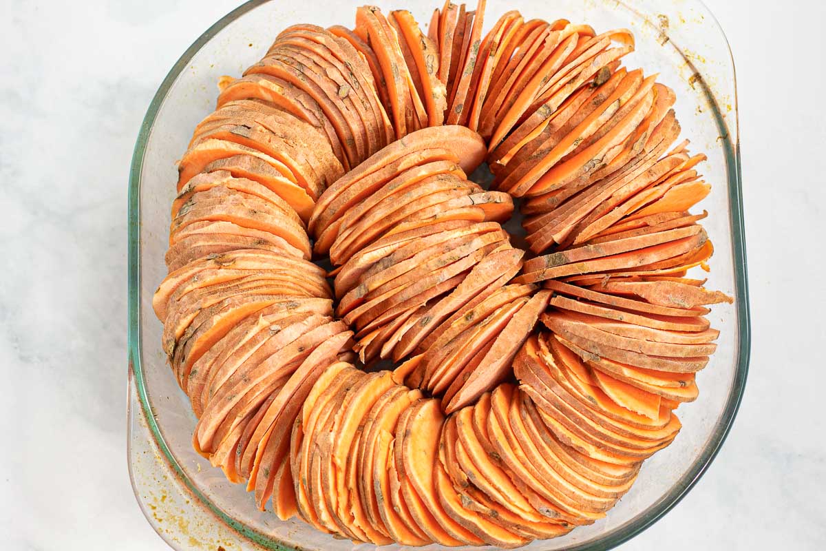 Thinly sliced sweet potatoes arranged in a roasted dish.