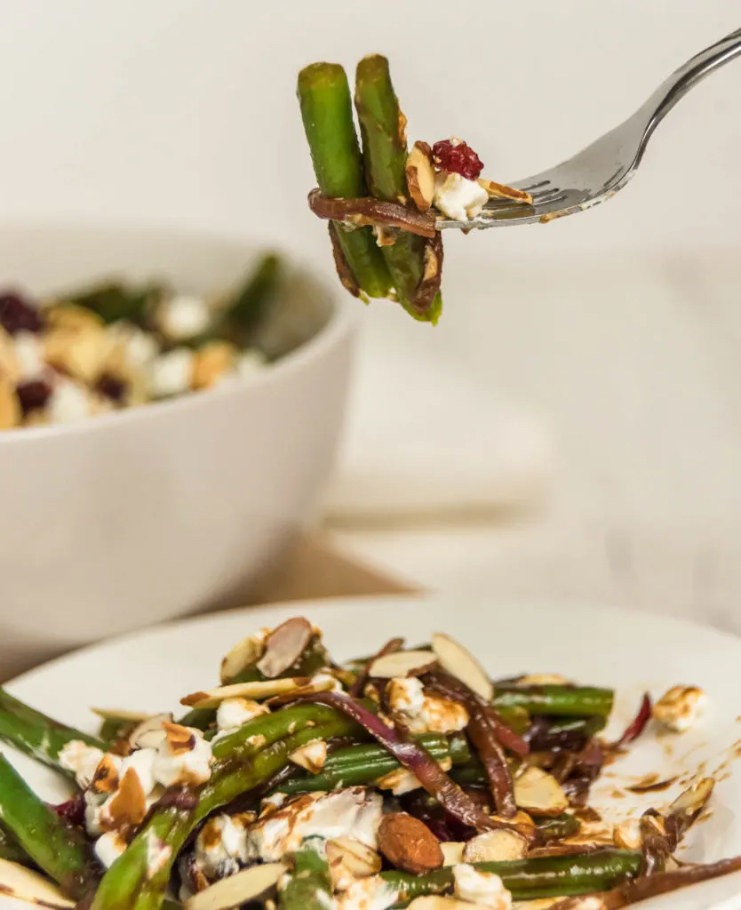 Fork picking up green beans with almonds and goat cheese.