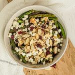 Bowl of green bean side dish with cranberries, almonds, and goat cheese.