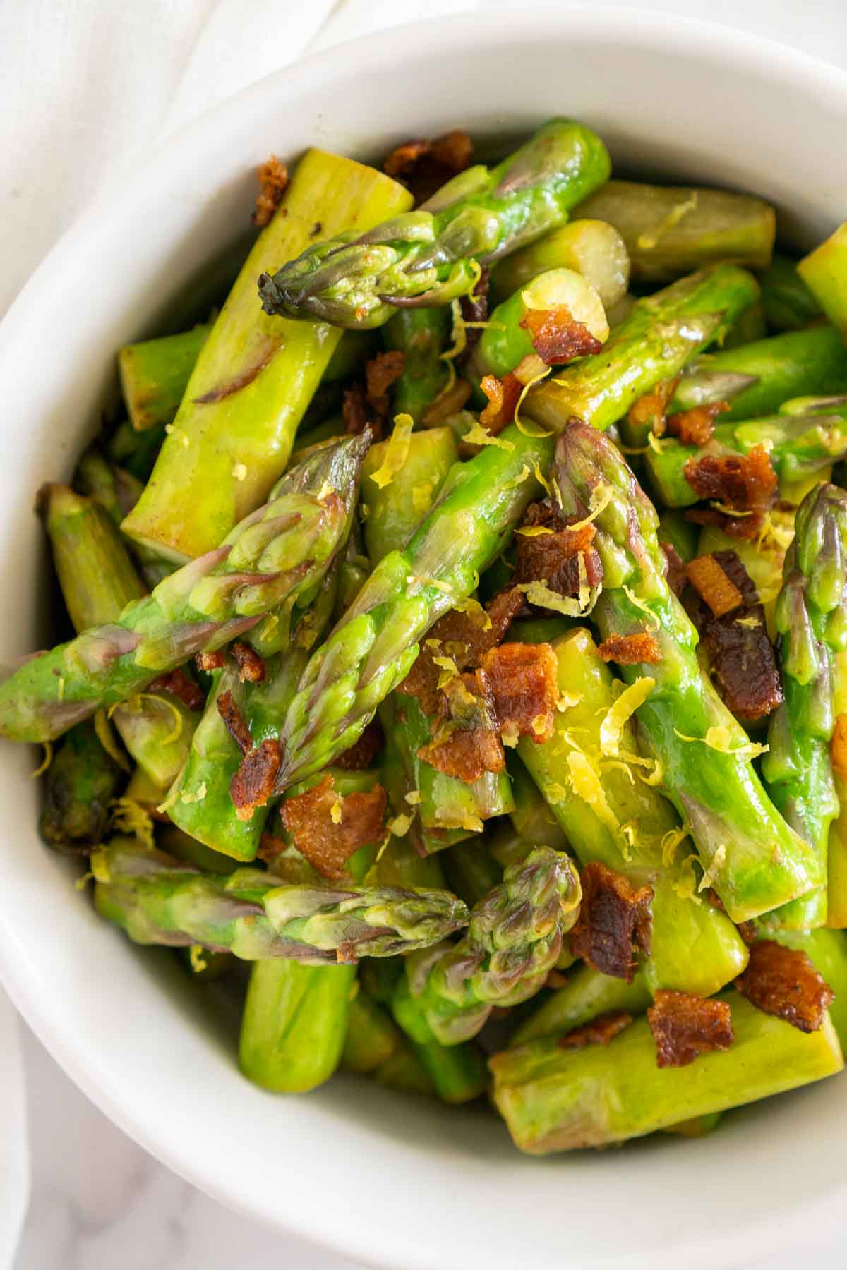 Bowl of cooked asparagus with bacon and lemon zest