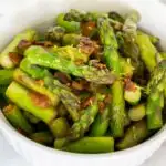 Bowl of chopped pan fried asparagus with bacon bits and lemon zest
