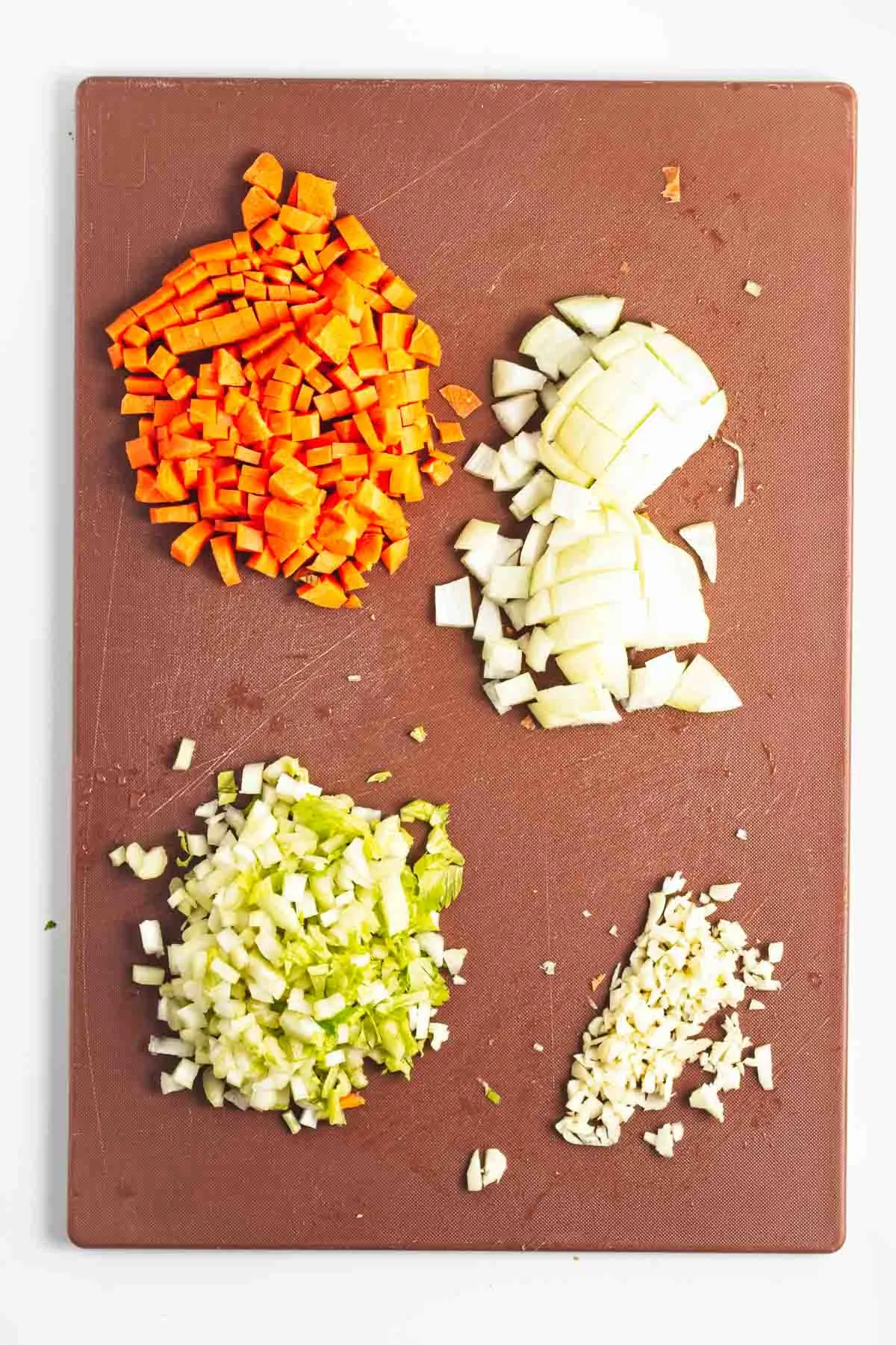 Diced carrots, celery, onion, and garlic on a cutting board.