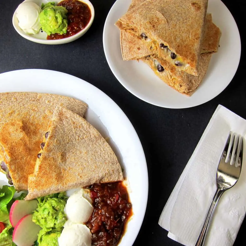 black bean pulled pork quesadilla on a plate with sour cream, guacamole, and salsa