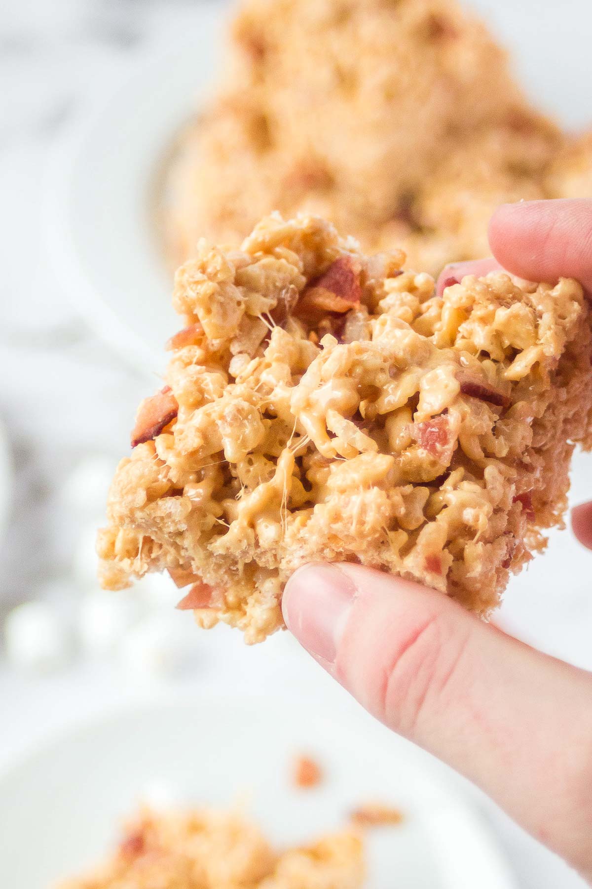 Hand holding gooey peanut butter rice krispies treat with bacon. 