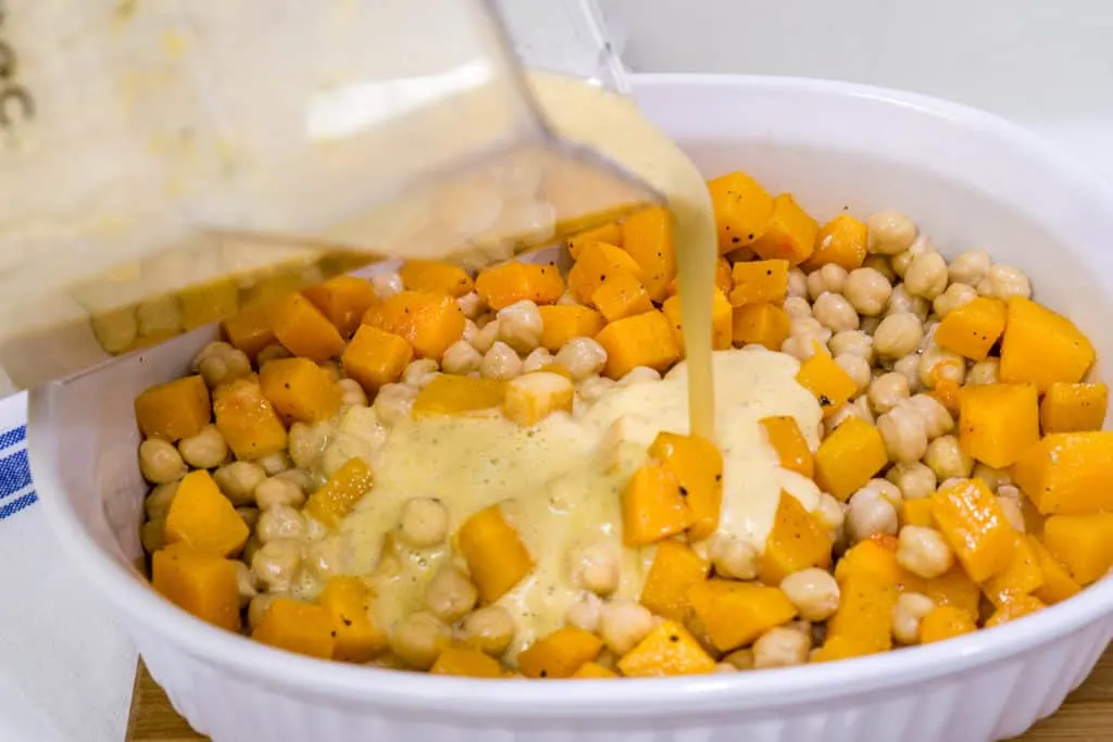 pouring sauce over thanksgiving chickpeas with butternut squash casserole