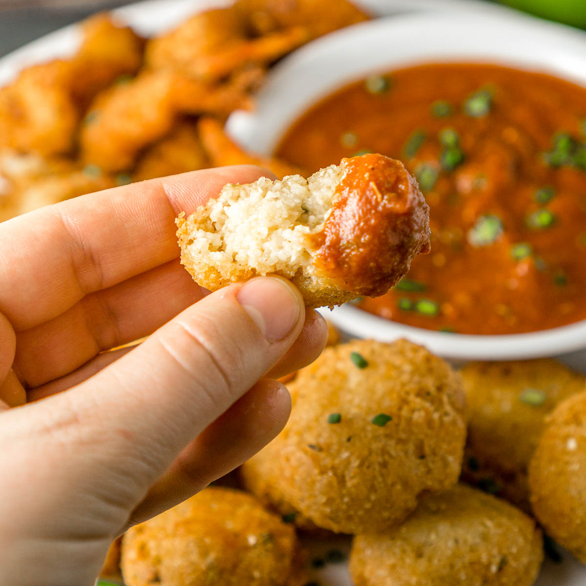Hand holding a grits fritter appetizer that's been bitten into.