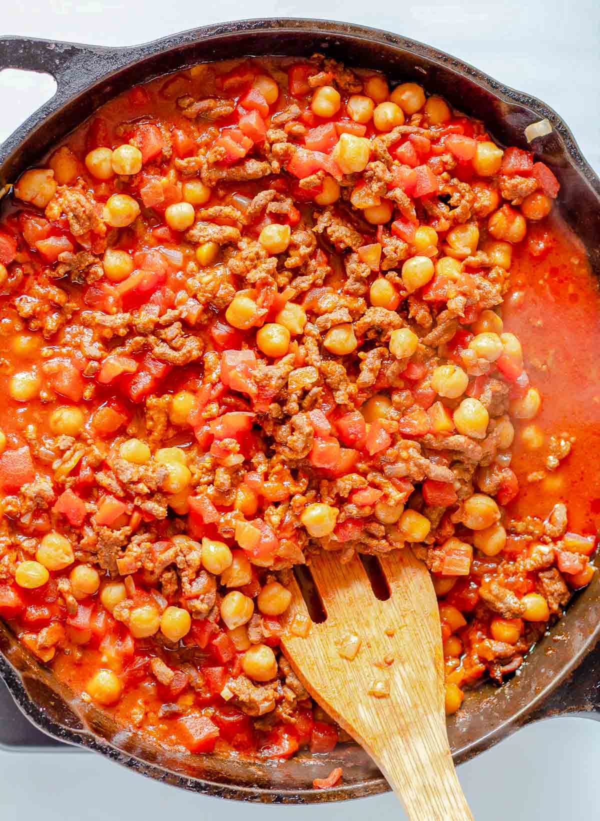 Chickpeas and chorizo stewing in a skillet with tomato sauce.