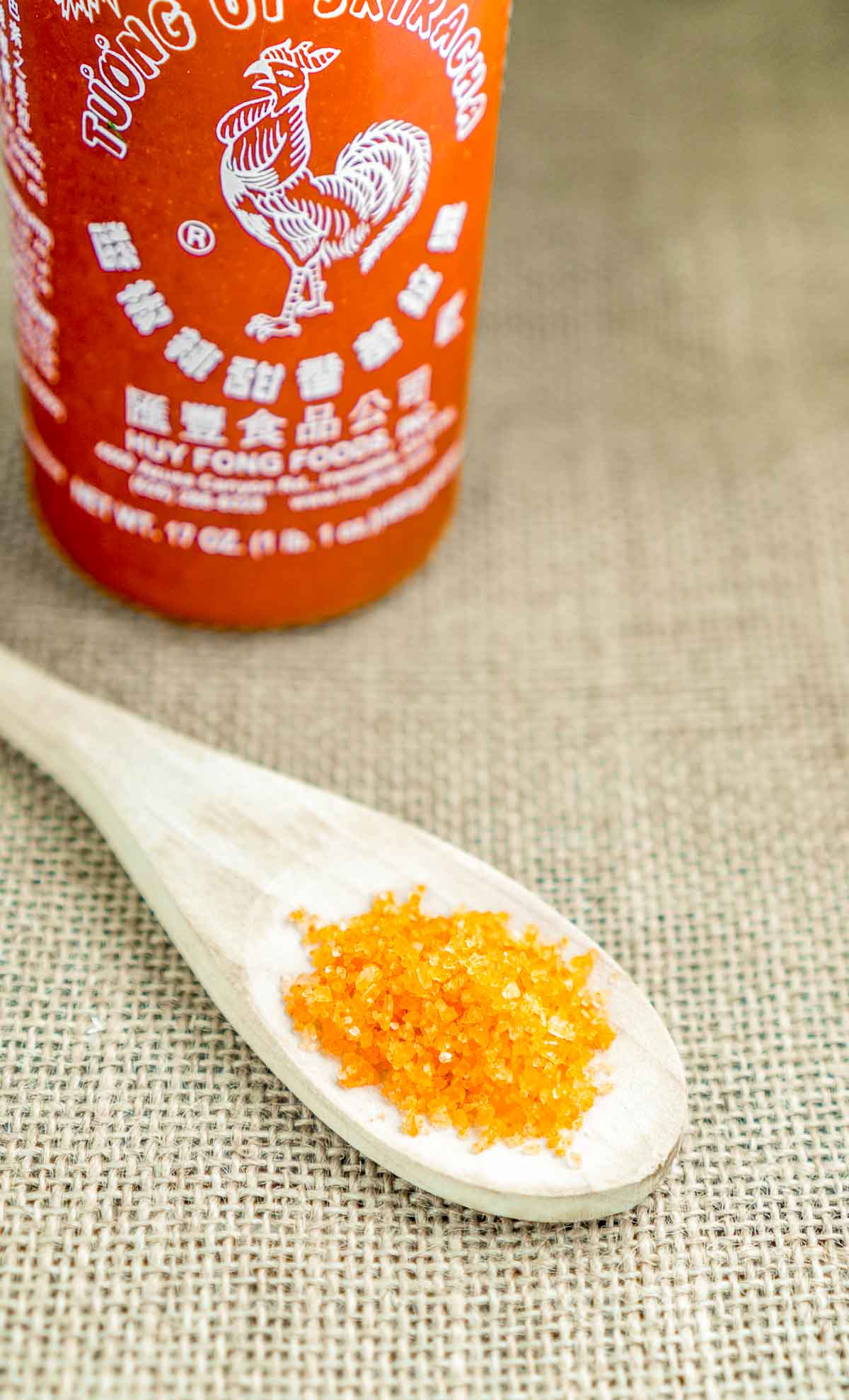 Sriracha finishing salt on a spoon with a bottle of sriracha behind it