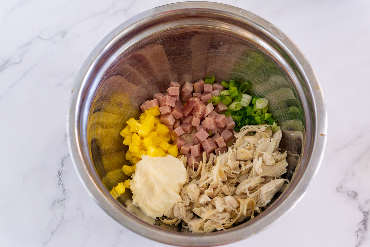 bowl of ingredients for chicken salad: pineapple, ham, scallions, mayo, diced chicken