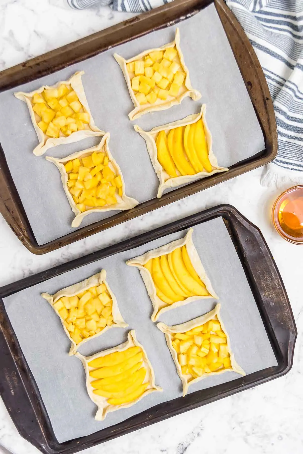 Puff pastry squares loaded with mango and pineapple on a baking sheet
