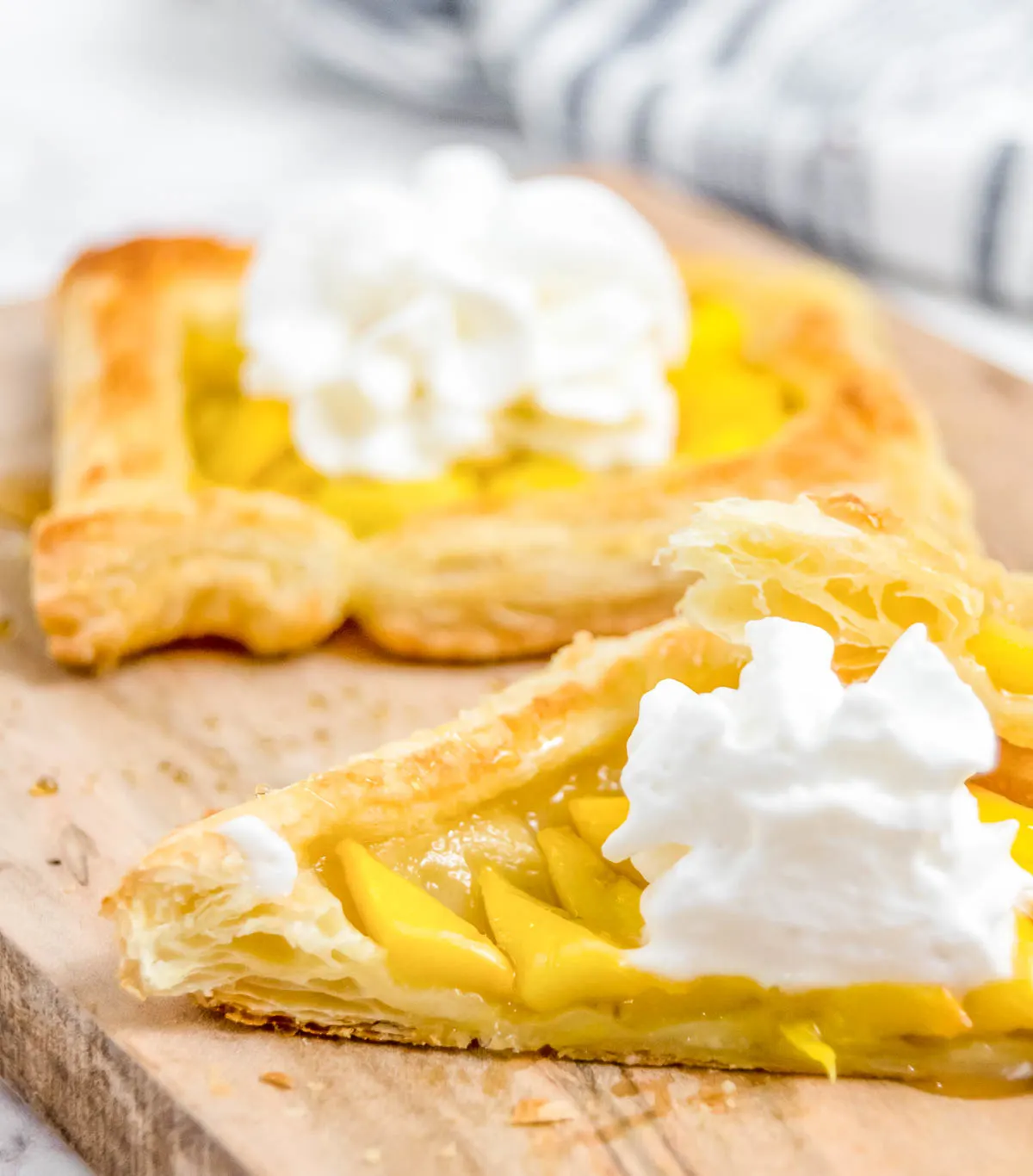 Mango puff topped with whipped cream cut in half to show flaky texture