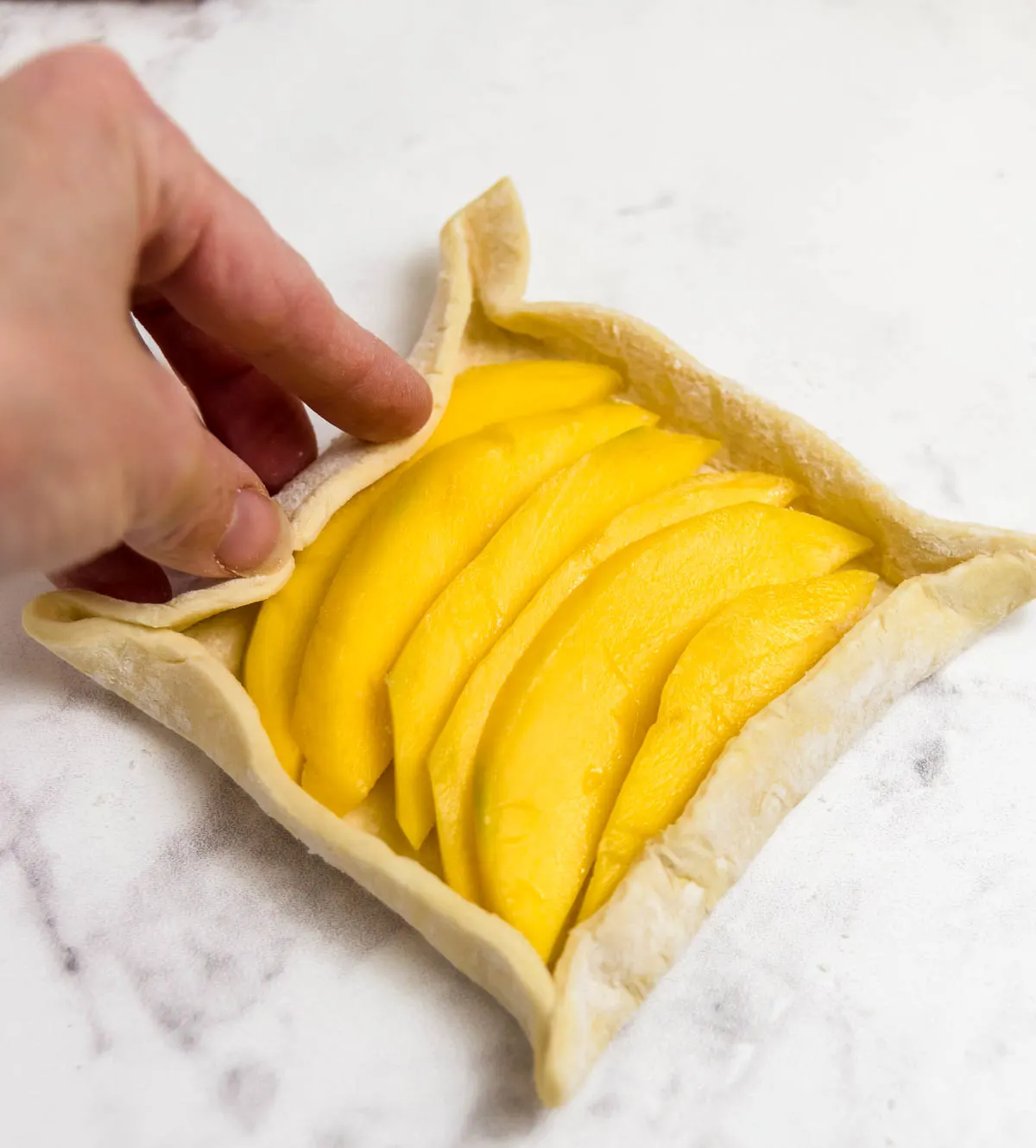 Adding sliced mango to puff pastry squares
