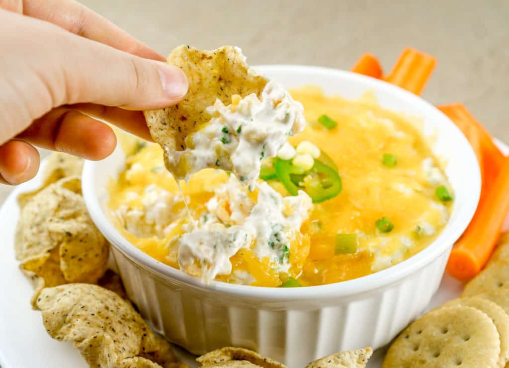 hand dipping corn chip into cheesy corn dip with cream cheese