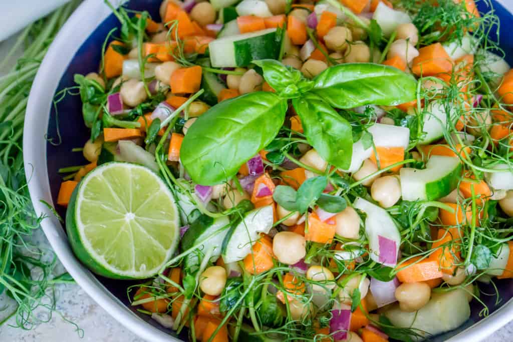 Bowl of chickpea and pea shoots salad with chopped vegetables.