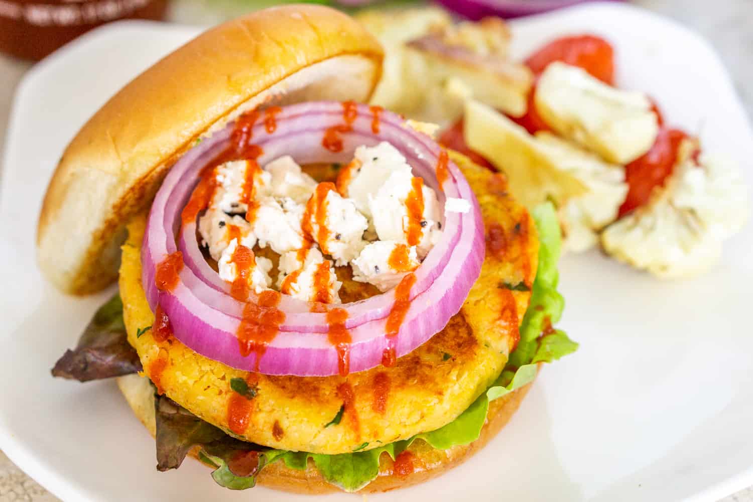 chickpea sweet potato burgers topped with feta, sriracha, and red onion