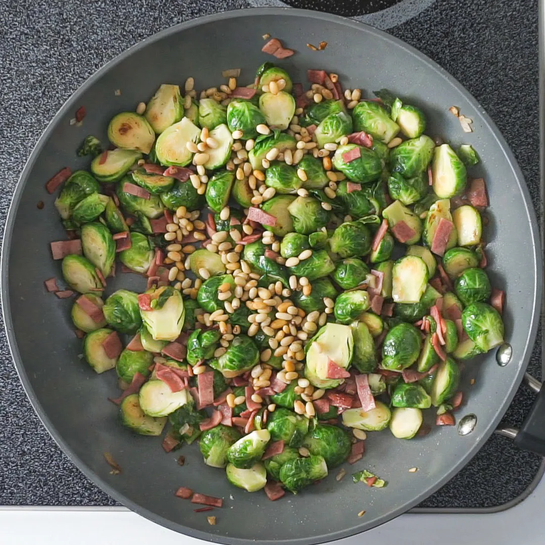 pan fried brussels sprouts, turkey bacon, and pine nuts in a pan