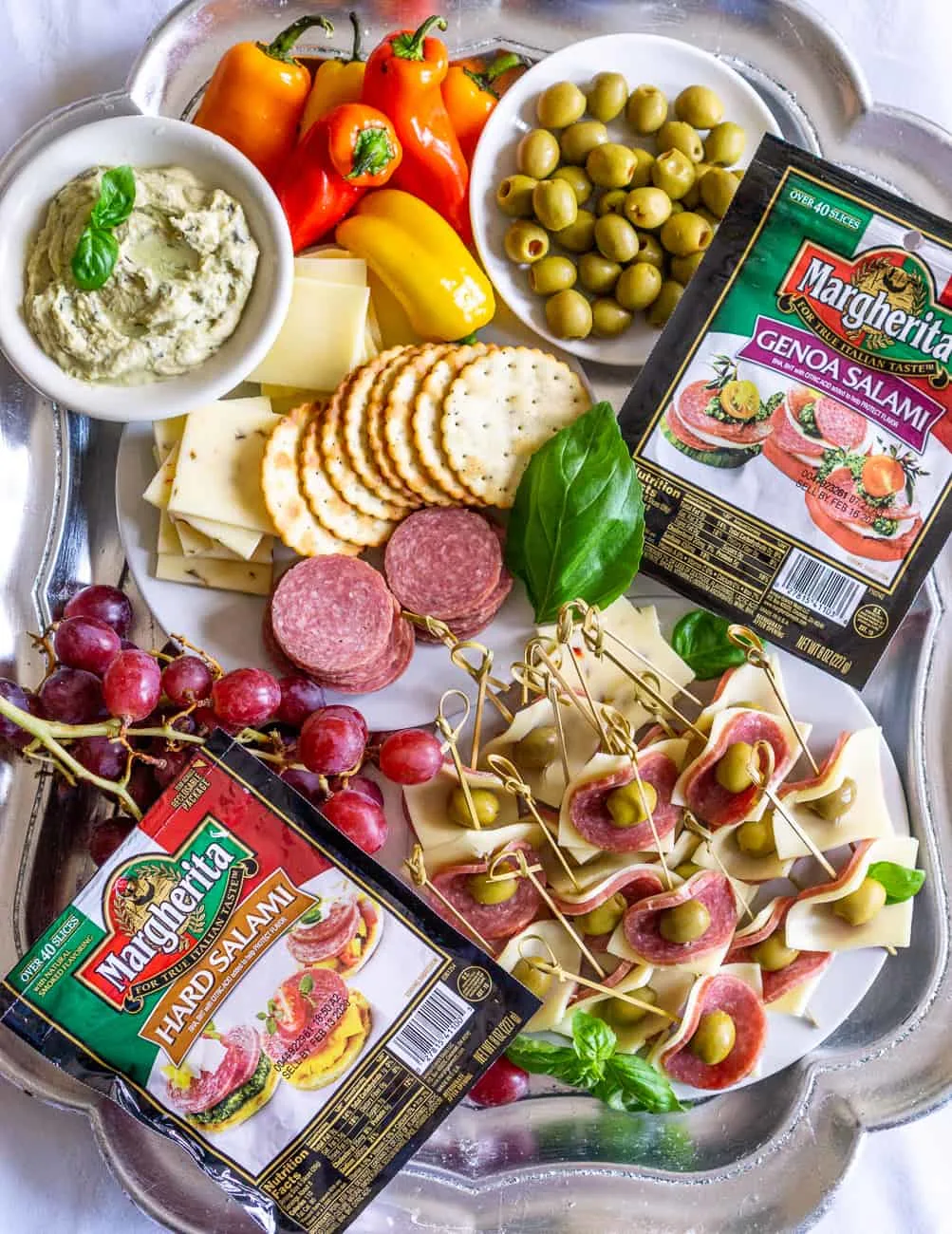 appetizer tray with a plate of salami appetizers, hummus, crackers, salami, cheese, grapes