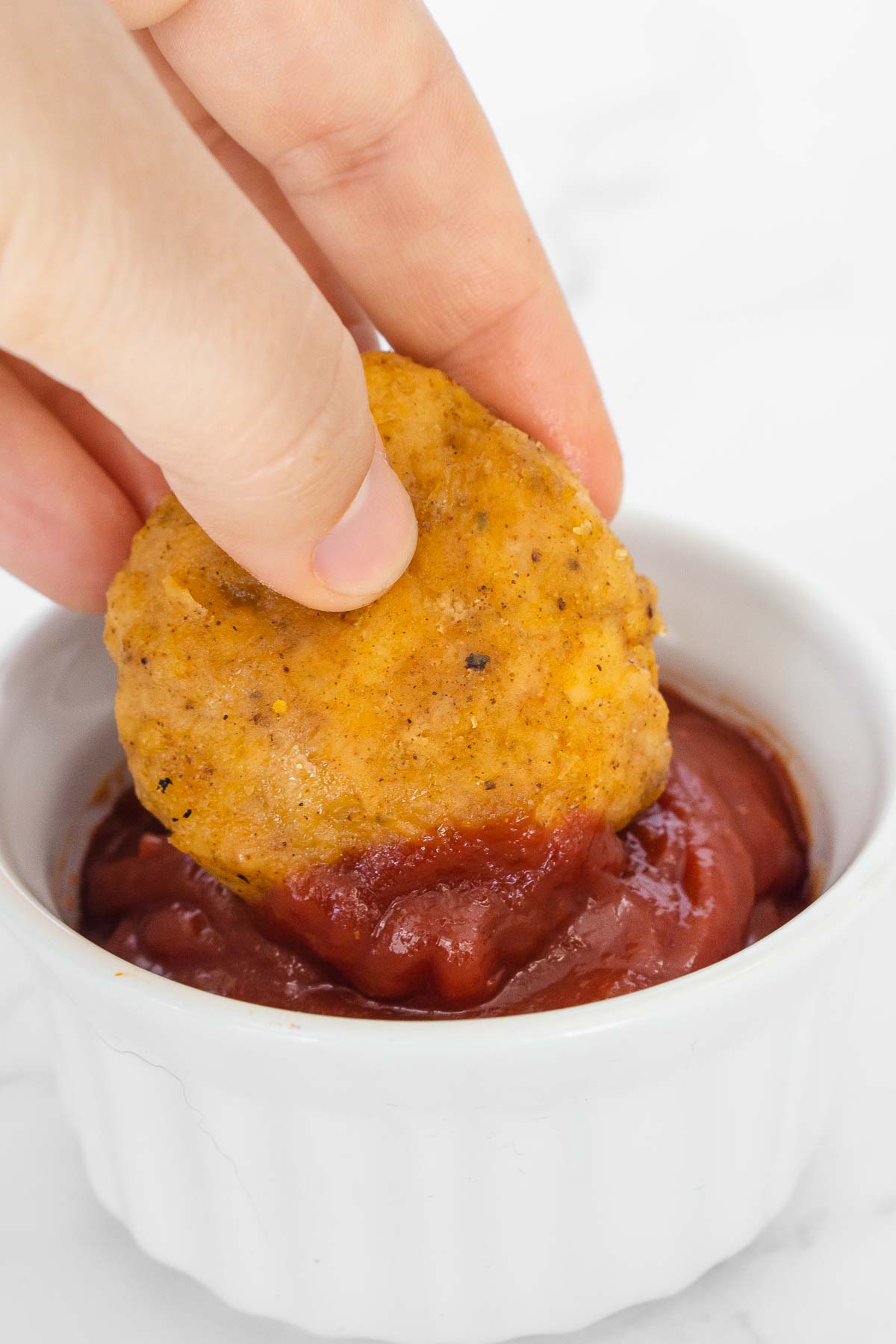 Hand dipping sweet potato chicken nugget in ketchup.