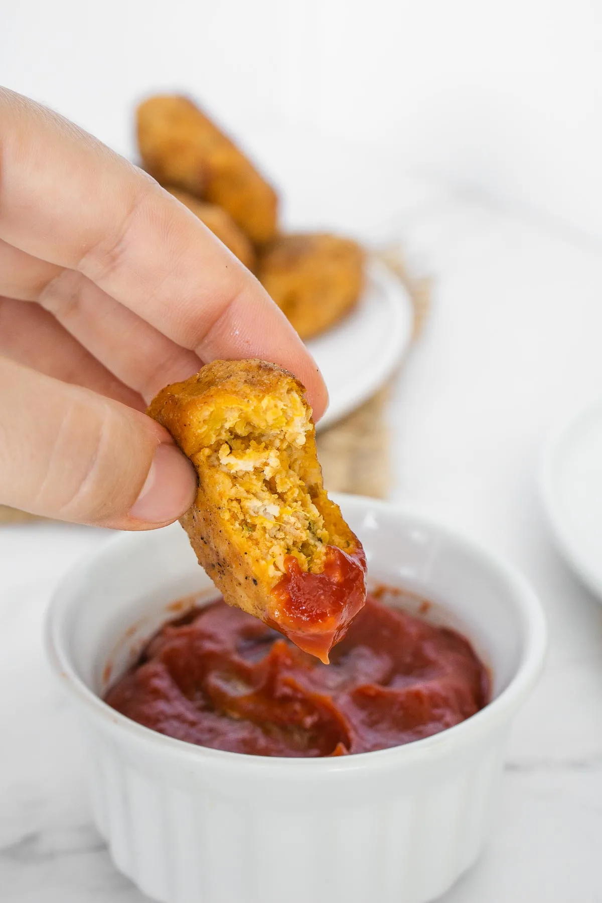 Showing the inside of a sweet potato chicken nugget that's dipped in ketchup.