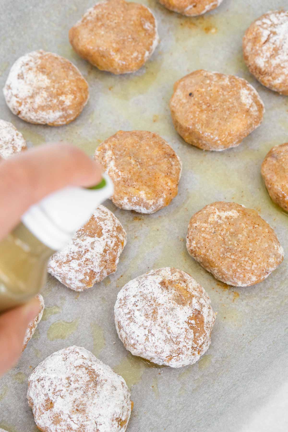 Spraying olive oil on unbaked nuggets.