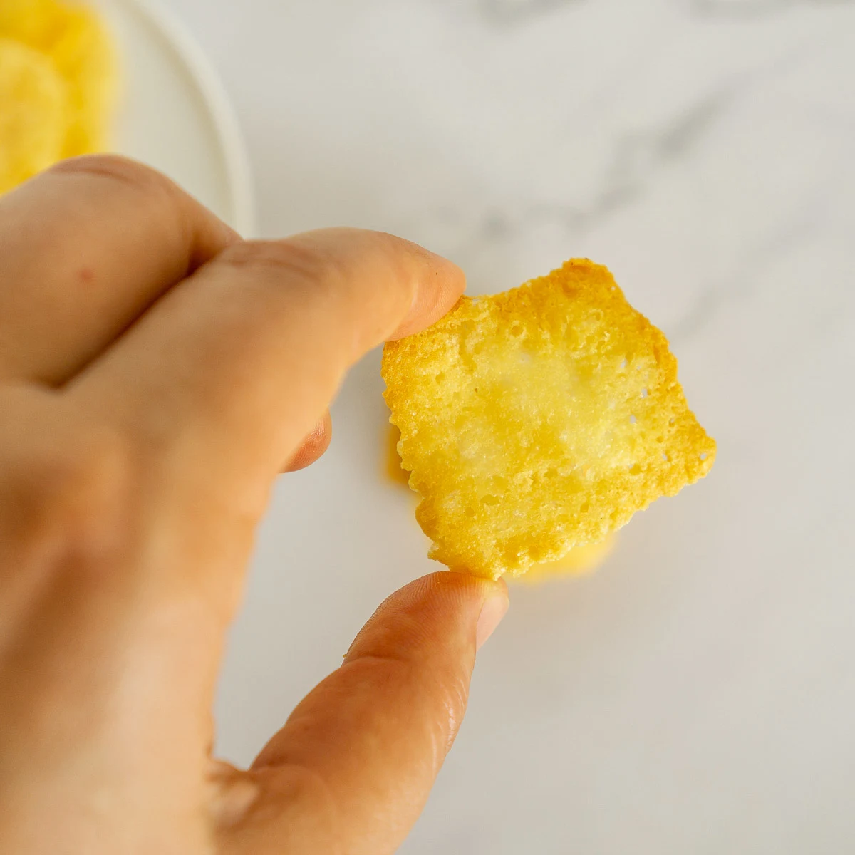 Hand holding asiago cheese crisp.