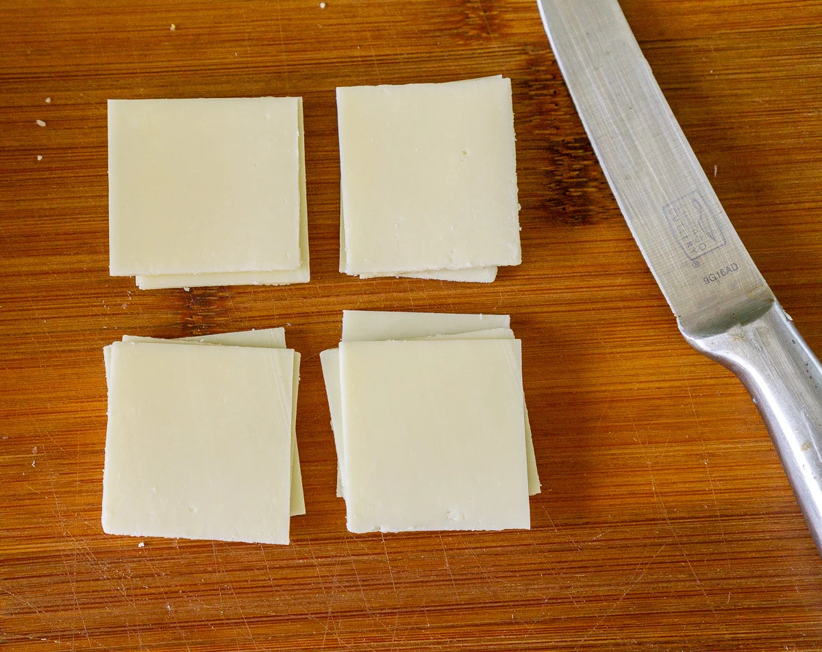 Sliced Asiago cheese on a cutting board.