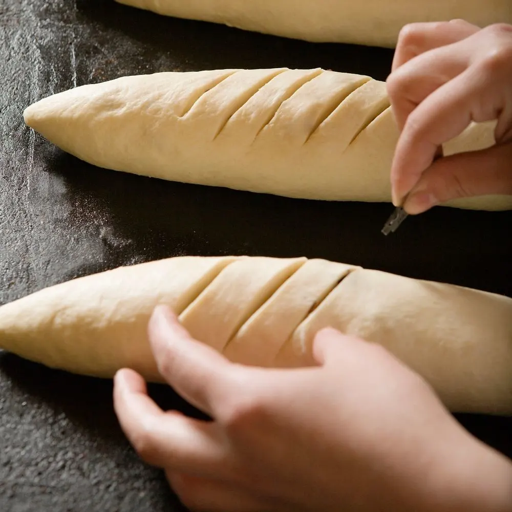 baker scoring baguettes before baking
