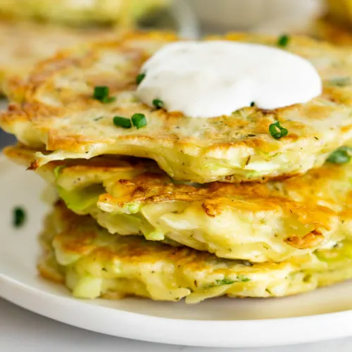 stack of cabbage fritters topped with sour cream sauce