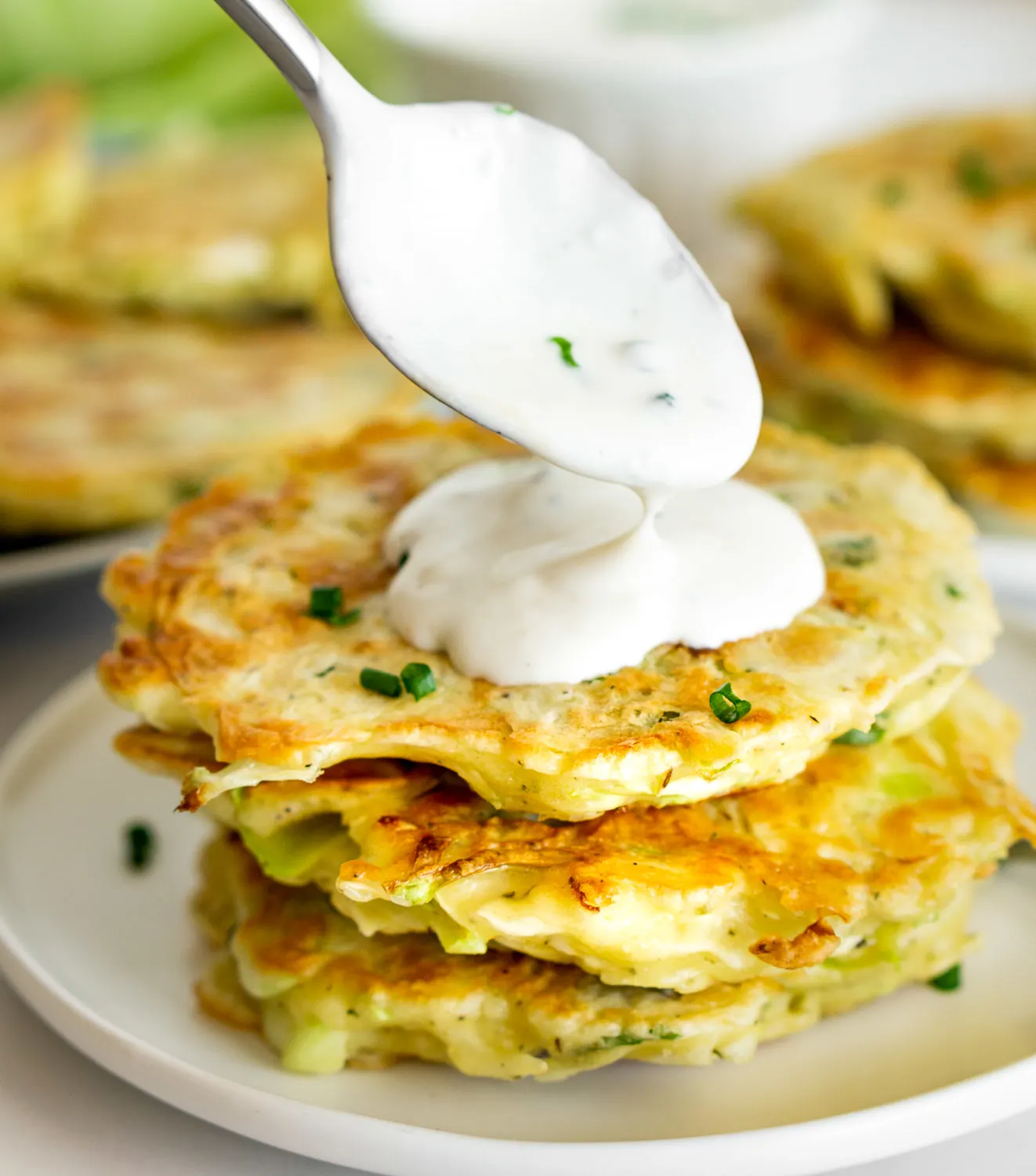 stack of cabbage fritters with sour crema being put on top with a spoon