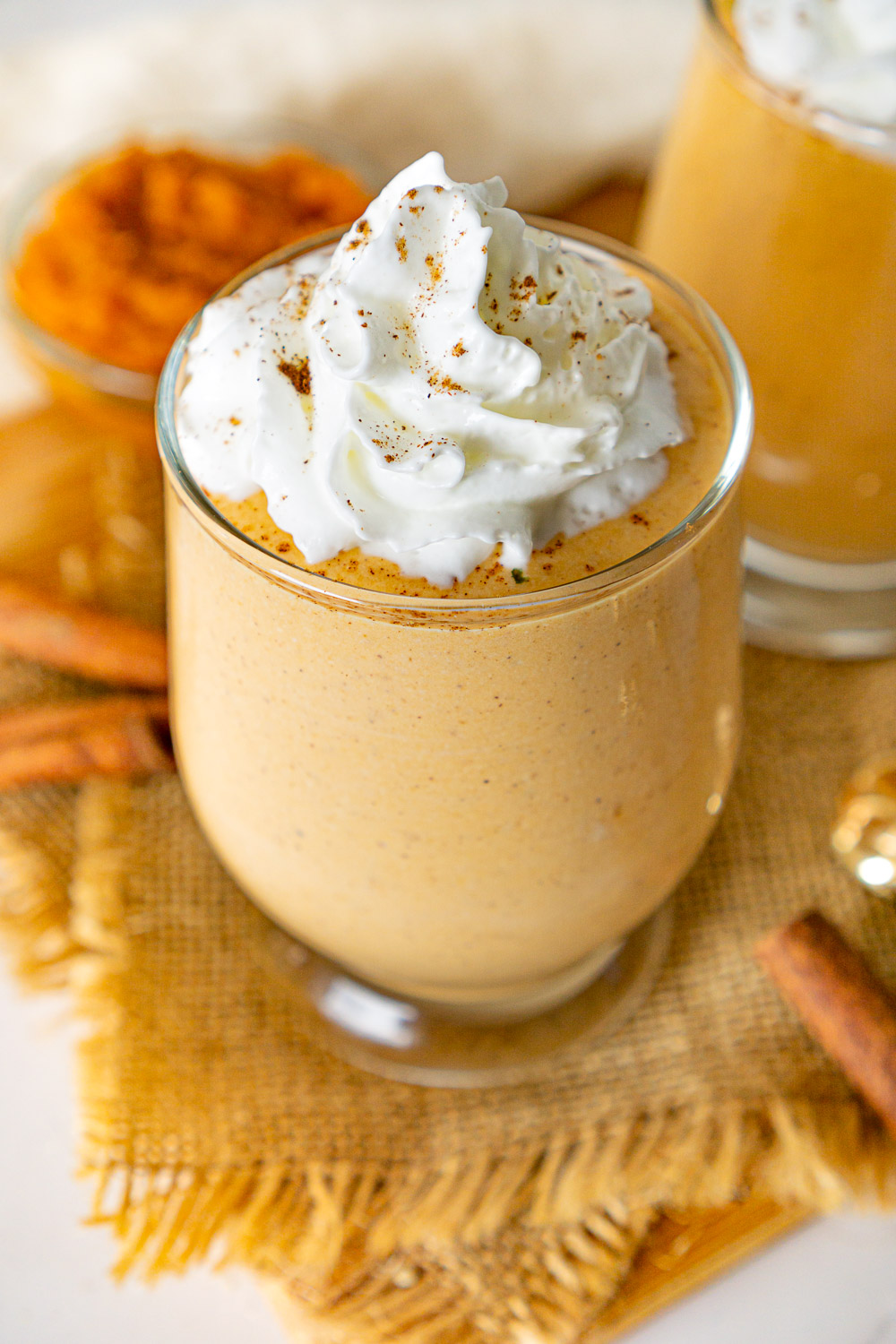 glass cup filled with pumpkin spice whipped cottage cheese and topped with whipped cream with pumpkin puree in the background