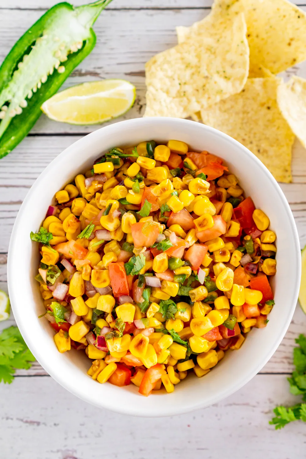charred corn salad in a bowl surrounded by jalapeno, lime, chips