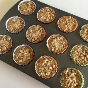 cinnamon muffin batter in a muffin pan, topped with crumb topping