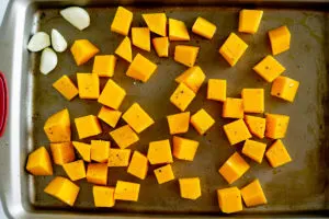 butternut squash and garlic cloves on a roasting pan