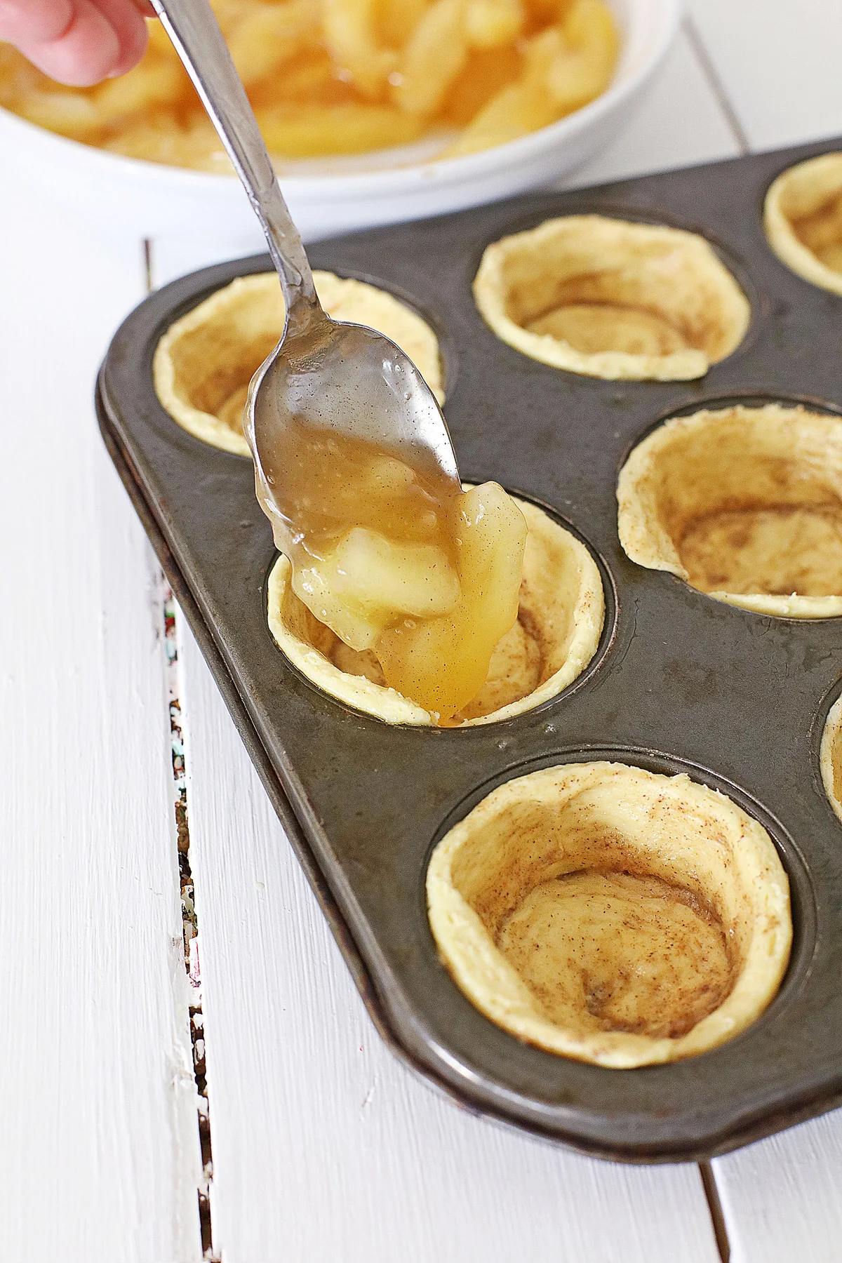 spooning apple pie filling into cinnamon muffin cups