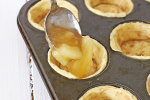 spooning apple pie filling into cinnamon roll muffin cups