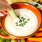 hand dipping cucumber into creamy garlic dip - a low carb keto appetizer