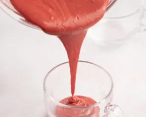 pouring red velvet cake batter into a mug